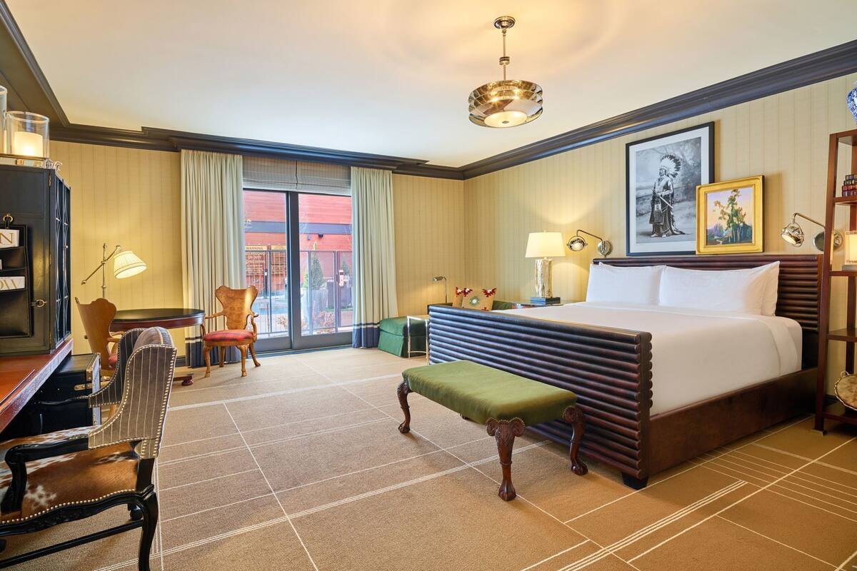 Une chambre d’hôtel avec un grand lit, un bureau, une chaise, un banc, une lampe et un tableau au mur.