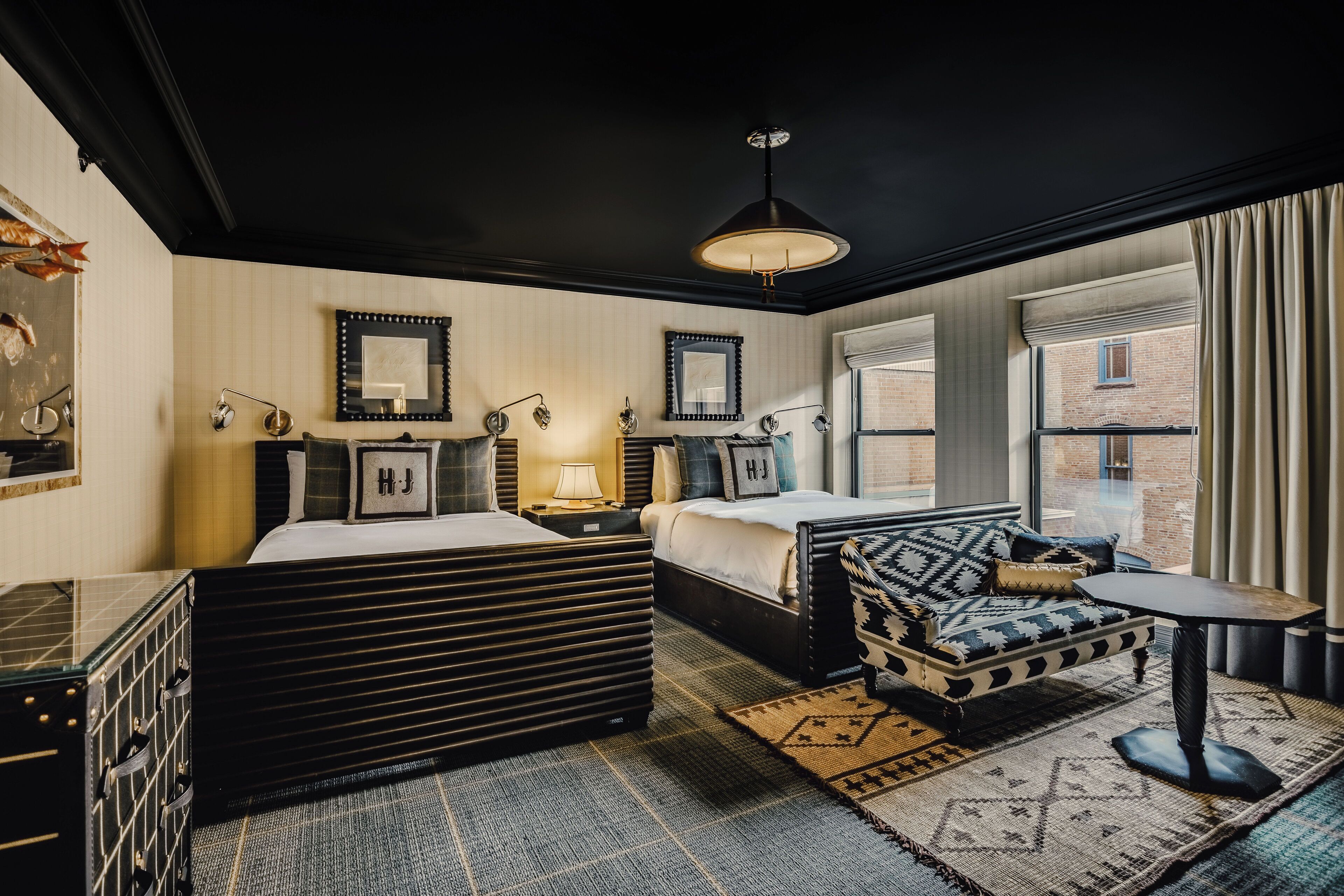 A modern hotel room with a large bed, a sofa, a small table, and a window with curtains.