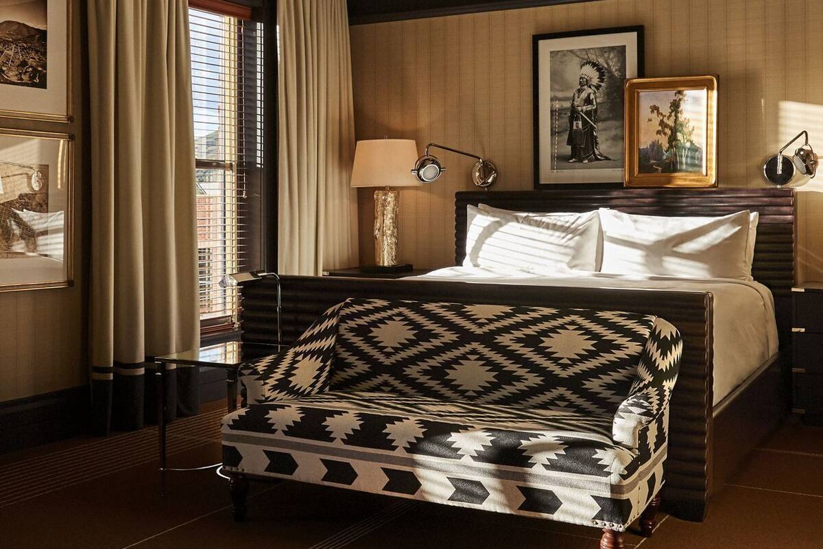 Une chambre d’hôtel avec un lit, un fauteuil à motifs, une table de chevet avec une lampe et des tableaux encadrés au mur.