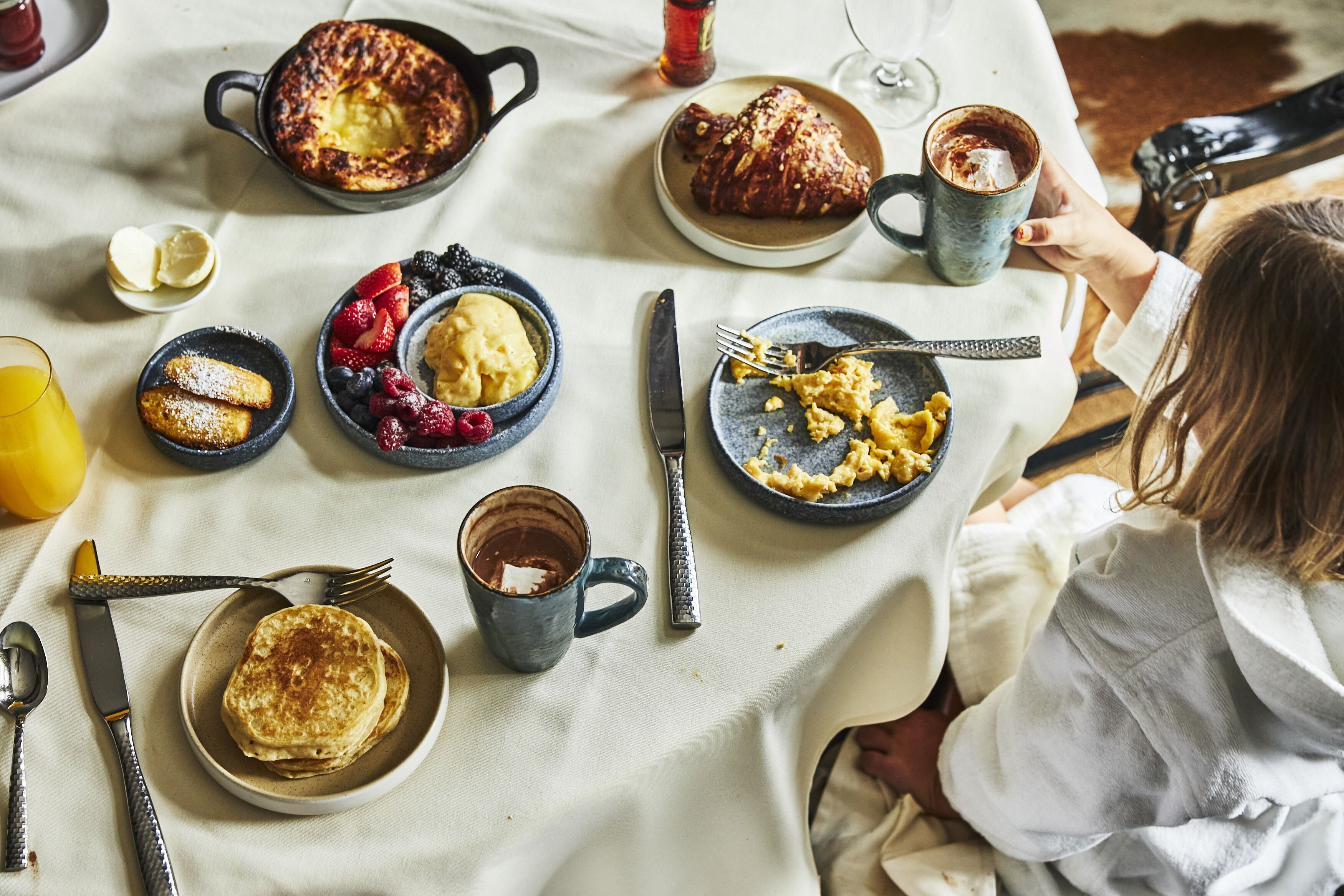 A breakfast table with various dishes, including pancakes, scrambled eggs, and a croissant.