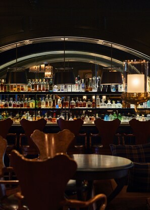 A bar with multiple shelves of liquor bottles, hanging lamps, and bar stools.