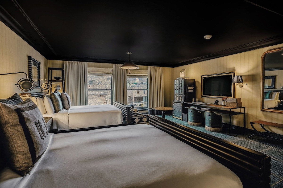 A hotel room with a large bed, a desk, a television, and a view of the city.