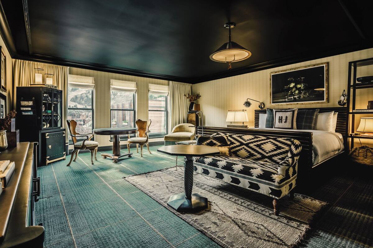 Une pièce comprenant un lit, un canapé, une table et une chaise. Il y a une fenêtre avec des rideaux, une lampe et un tableau encadré au mur.
