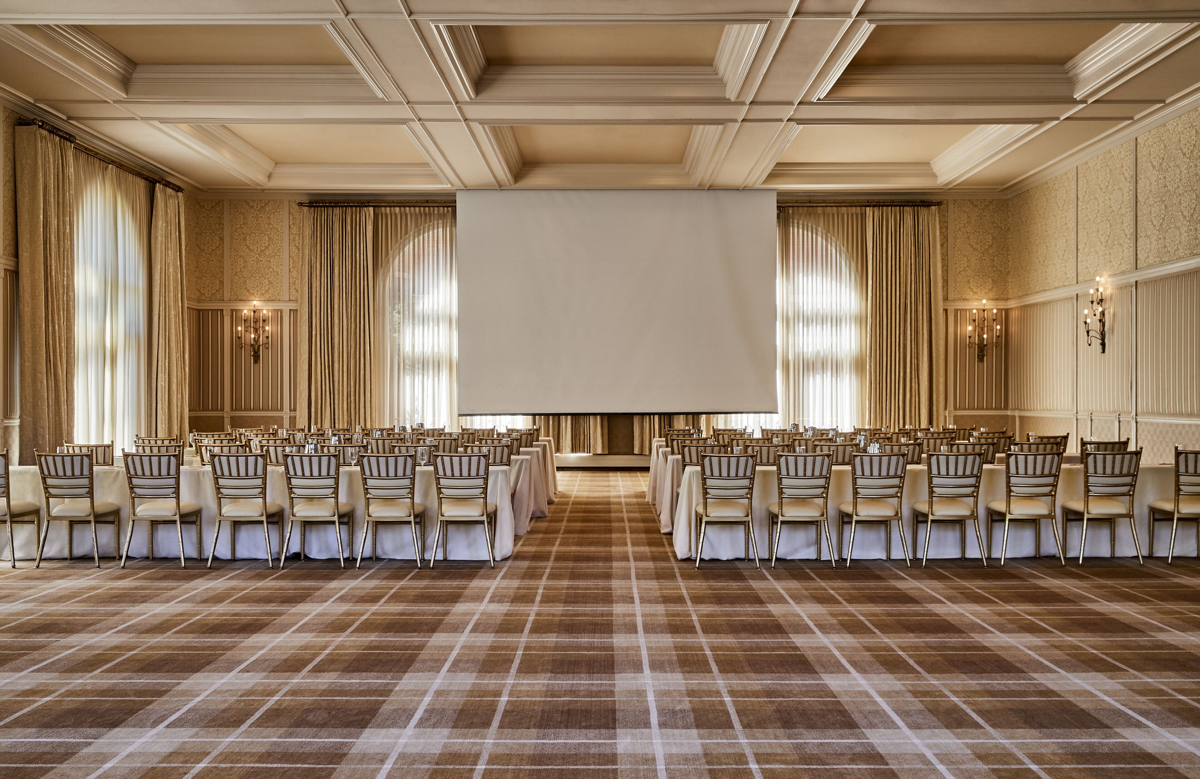 A large conference room with rows of chairs, a large screen, and elegant drapery.