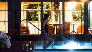A woman sitting by an indoor pool with a view of a restaurant in the background. - Hotel Jerome, Auberge Collection (Aspen)