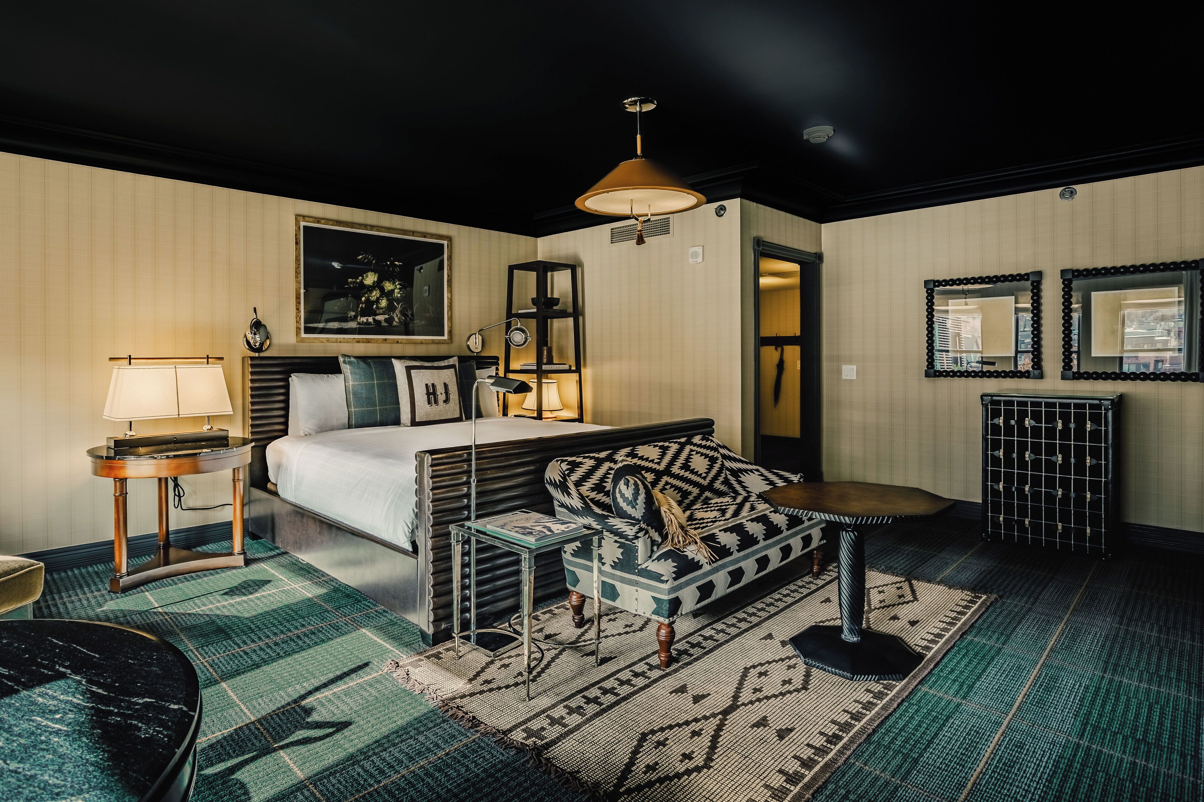 A hotel room with a bed, a sofa, a small table, a lamp, and a mirror.