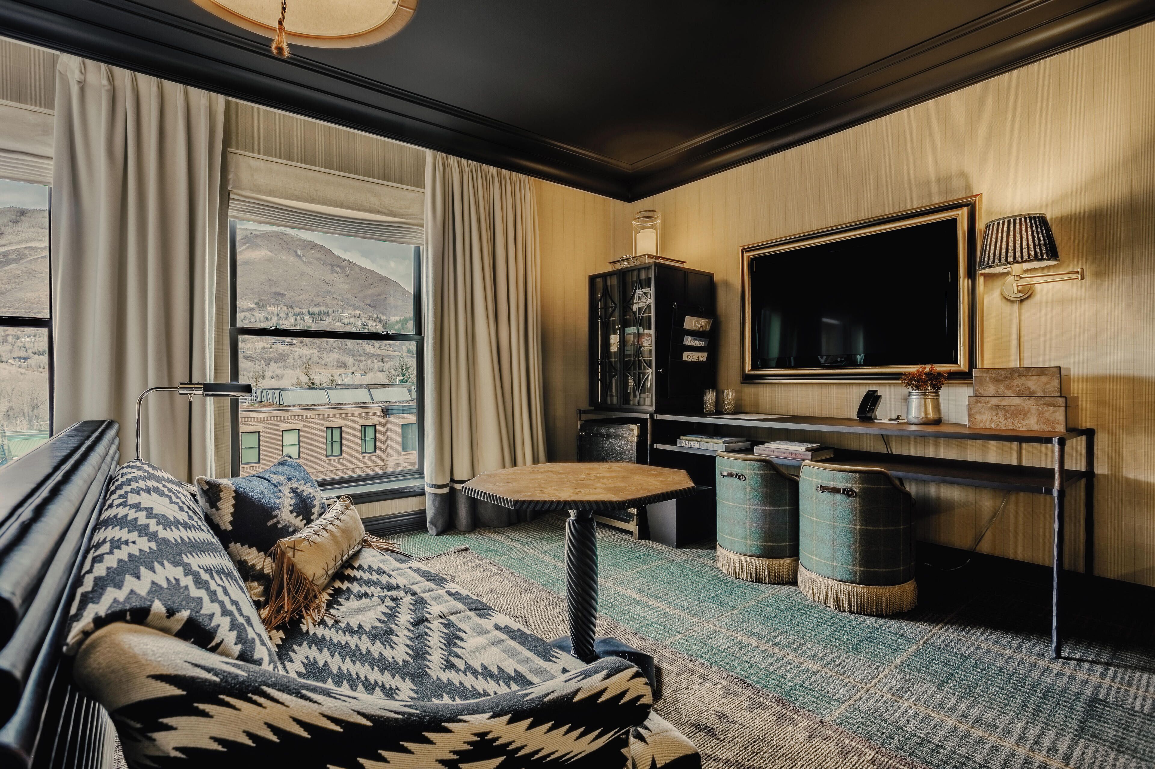 A cozy room with a sofa, a small table, a TV, and a view of a cityscape through large windows.