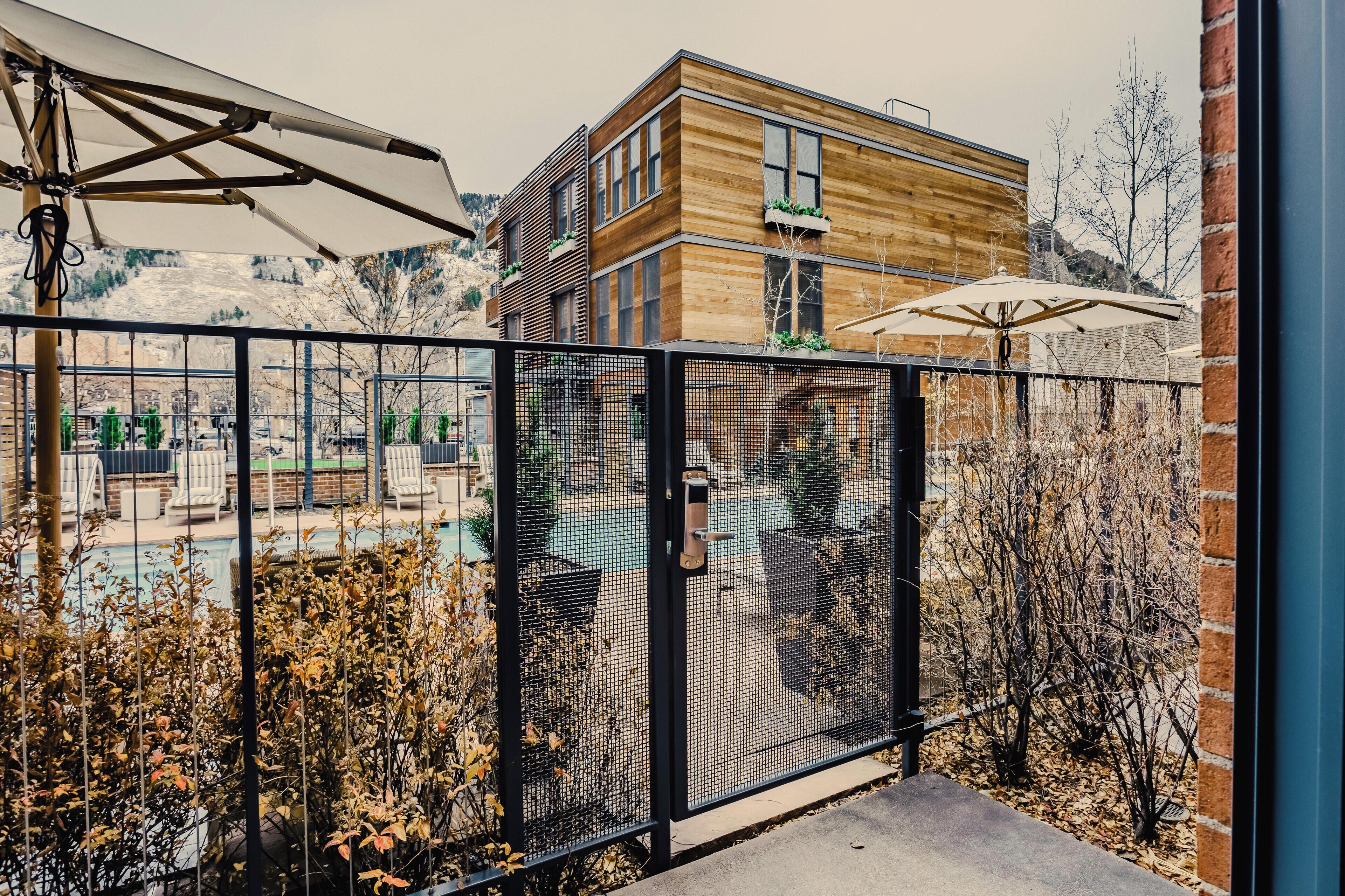 A modern building with a wooden facade, a fenced outdoor area with lounge chairs, and a view of a mountainous landscape.