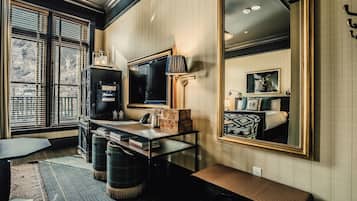 Une pièce avec un grand miroir, un bureau avec une lampe, un téléviseur et une fenêtre avec des stores.