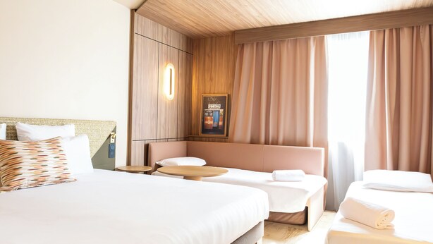Hotellihuoneessa on suuri sänky, pienempi sänky, sohva ja pöytä.