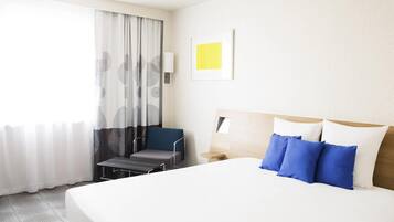 Una habitación de hotel con una cama grande, una silla, una mesita de noche y una ventana con cortinas.