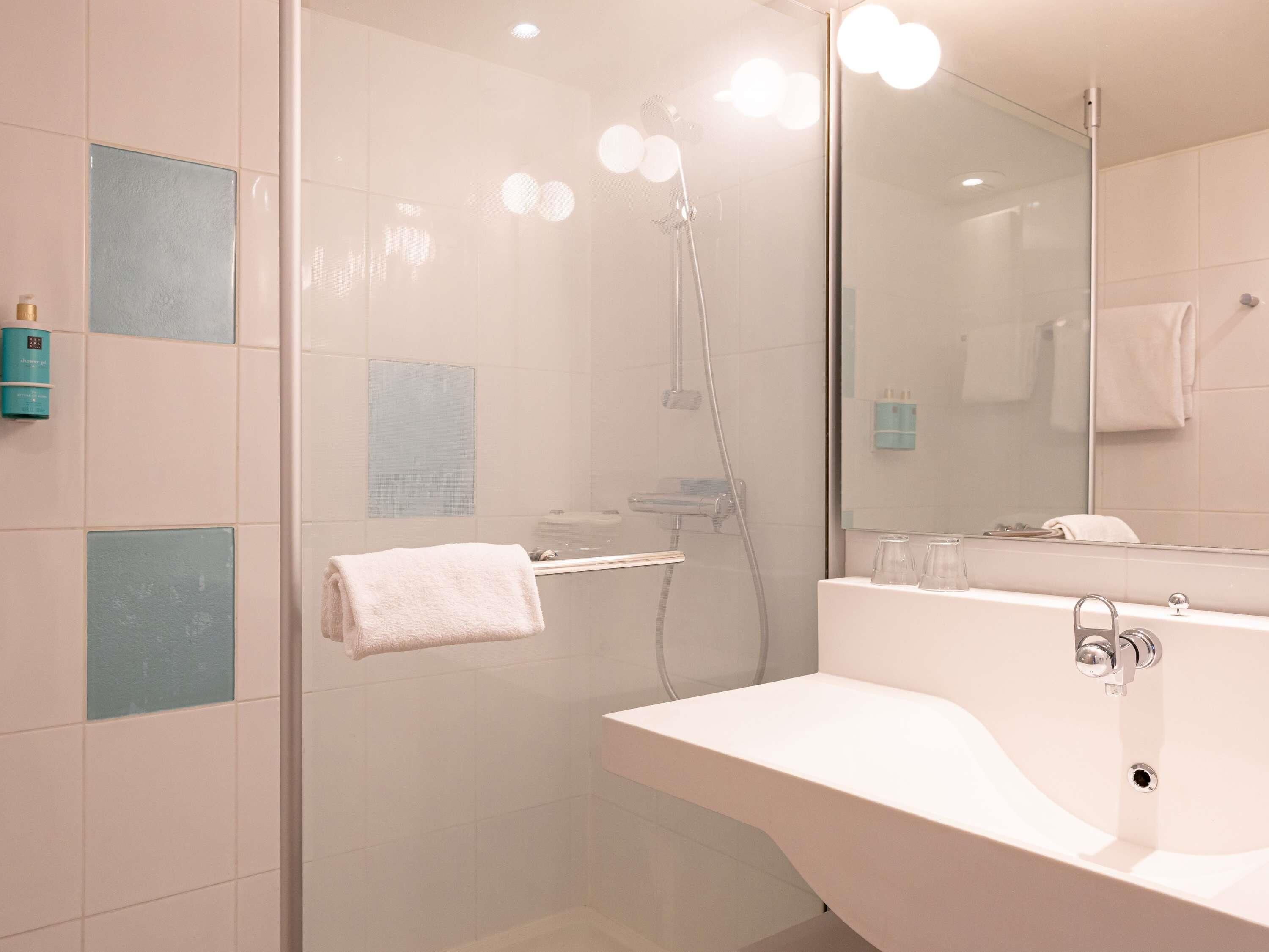 Une salle de bain moderne avec une douche à parois de verre, un lavabo blanc et un grand miroir.