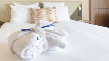 A neatly made bed with white linens, a patterned pillow, and a towel with a blue tag.