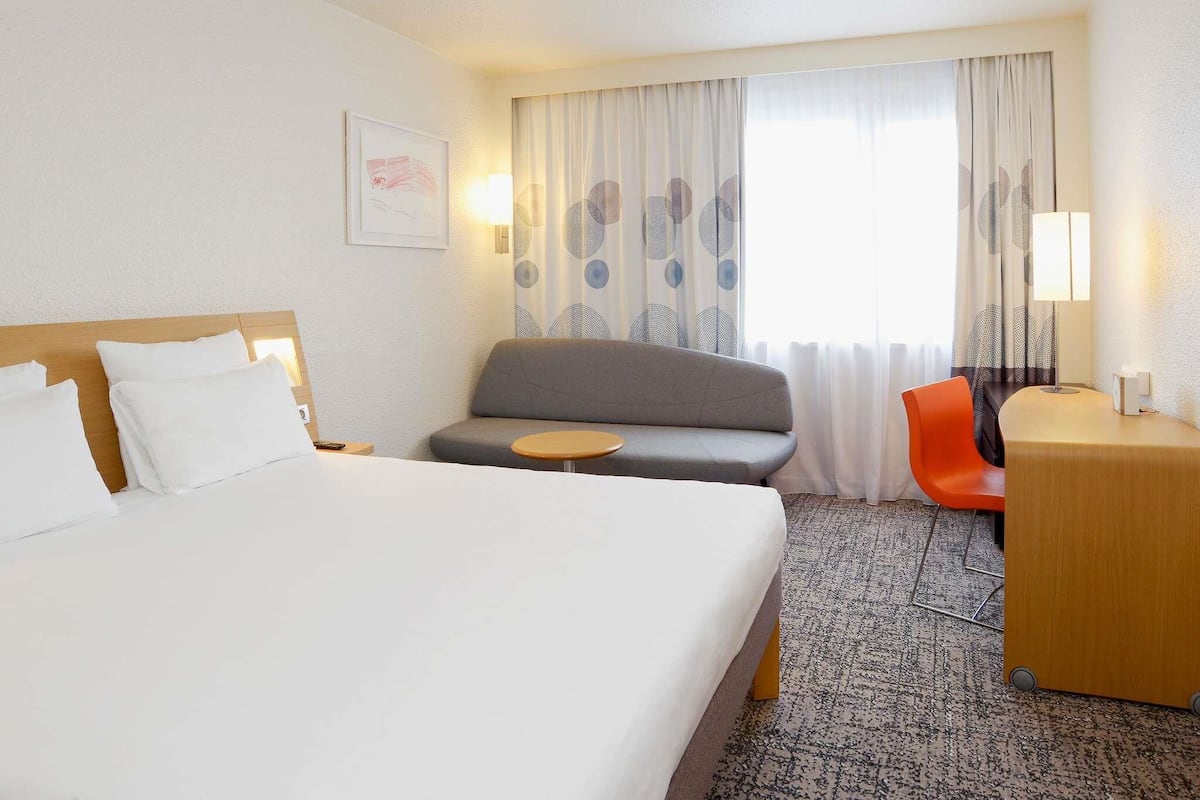A hotel room with a bed, a sofa, a small table, a desk, and a chair.