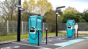 Dos estaciones de carga para vehículos eléctricos, identificadas con el rótulo 'Electra', con un área de estacionamiento cercada y flechas direccionales en el pavimento.