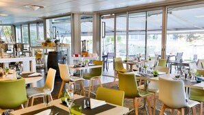 A modern restaurant with large windows, green and white chairs, and neatly arranged tables. - Novotel Toulouse Purpan Aéroport (Toulouse)