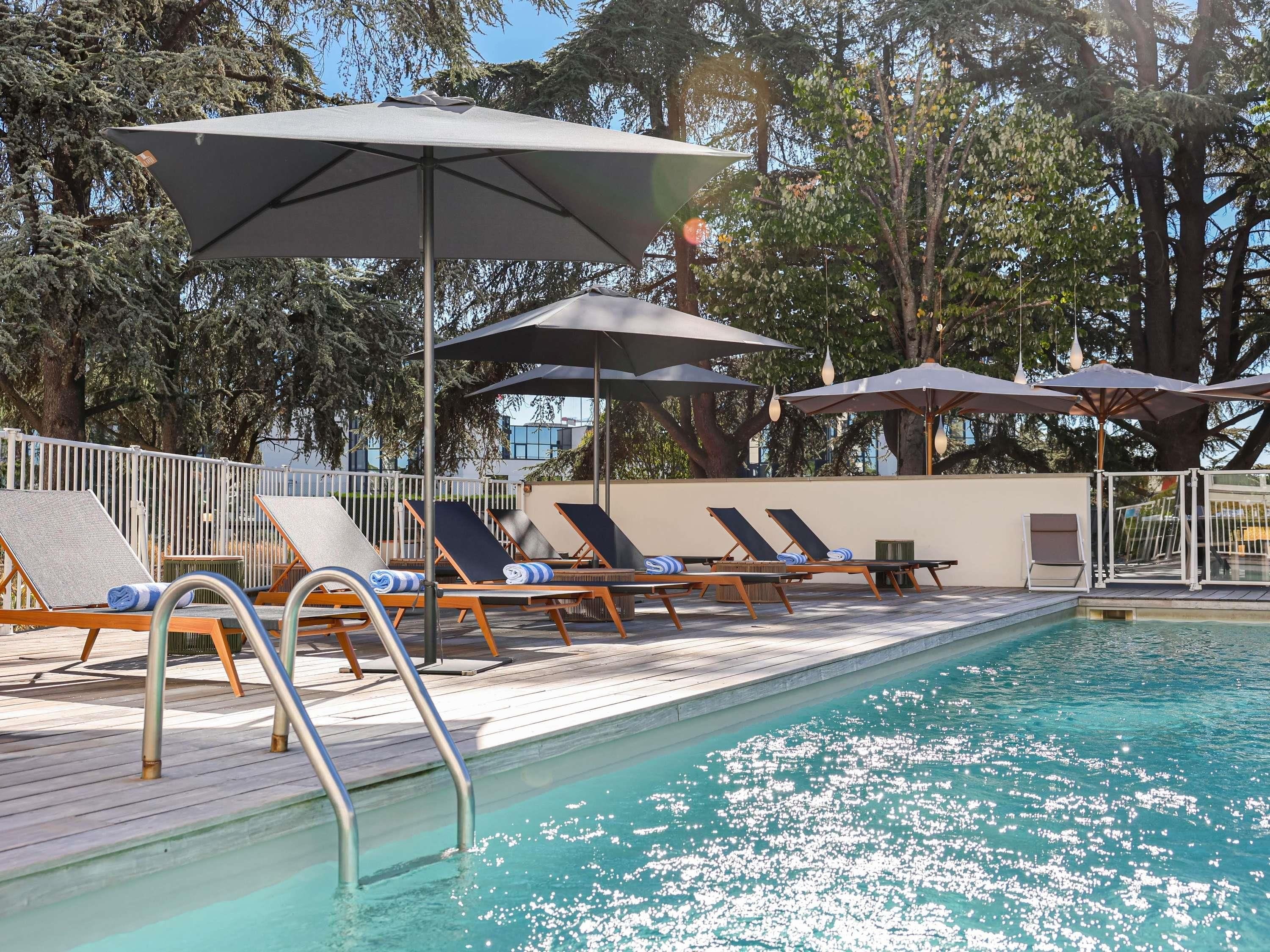 A poolside area with lounge chairs and umbrellas, surrounded by trees.
