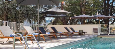A poolside area with lounge chairs and umbrellas, surrounded by trees.