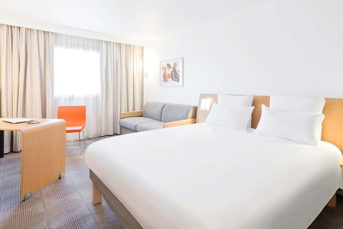 A hotel room with a large bed, a desk, an orange chair, and a sofa.
