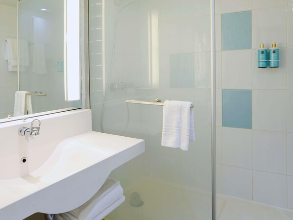 Un baño con lavamanos blanco, cabina de ducha de vidrio y toallero.