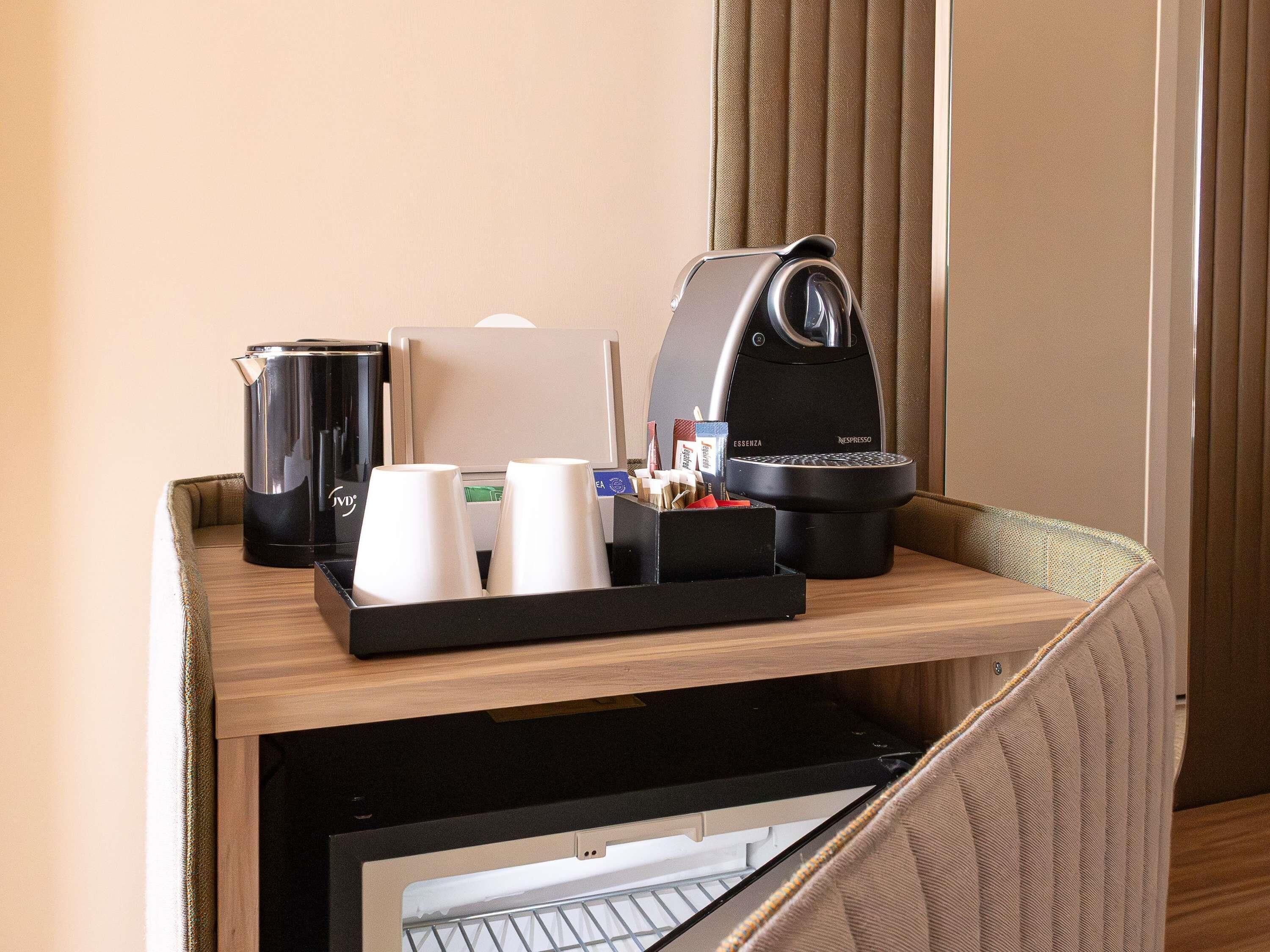 A hotel room's minibar with a coffee maker, a water dispenser, and a tray with cups and condiments.