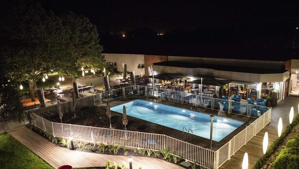 An outdoor pool area with a wooden deck, surrounded by a white fence and various seating arrangements. - Novotel Toulouse Purpan Aéroport (Toulouse)