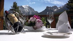 A table set with a bottle of wine, a glass, a vase of flowers, and a napkin, with a mountain view in the background. - Post Hotel and Spa (Lake Louise)