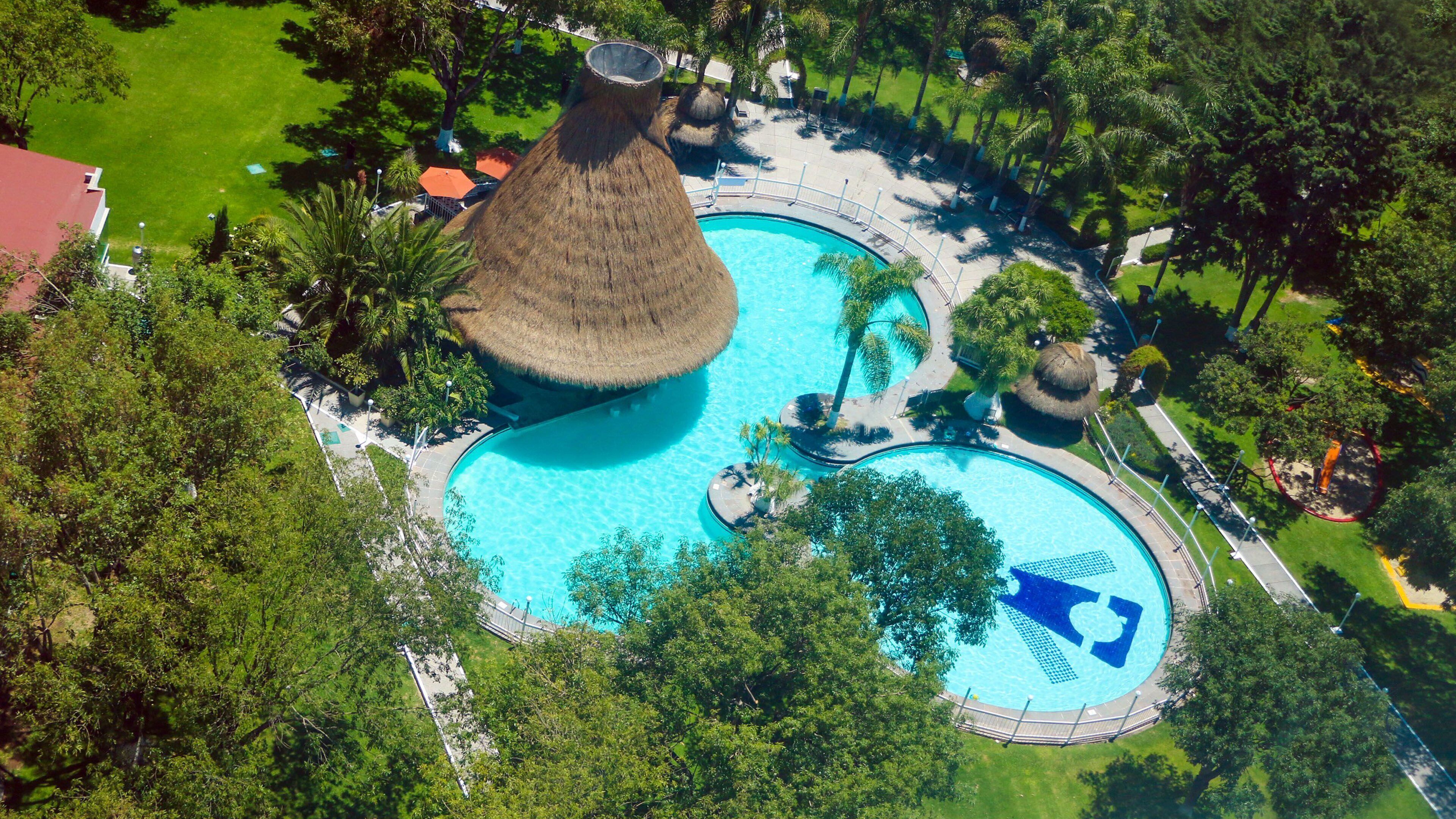 Vista aérea de un complejo turístico con múltiples piscinas, rodeado de exuberante follaje y palmeras.