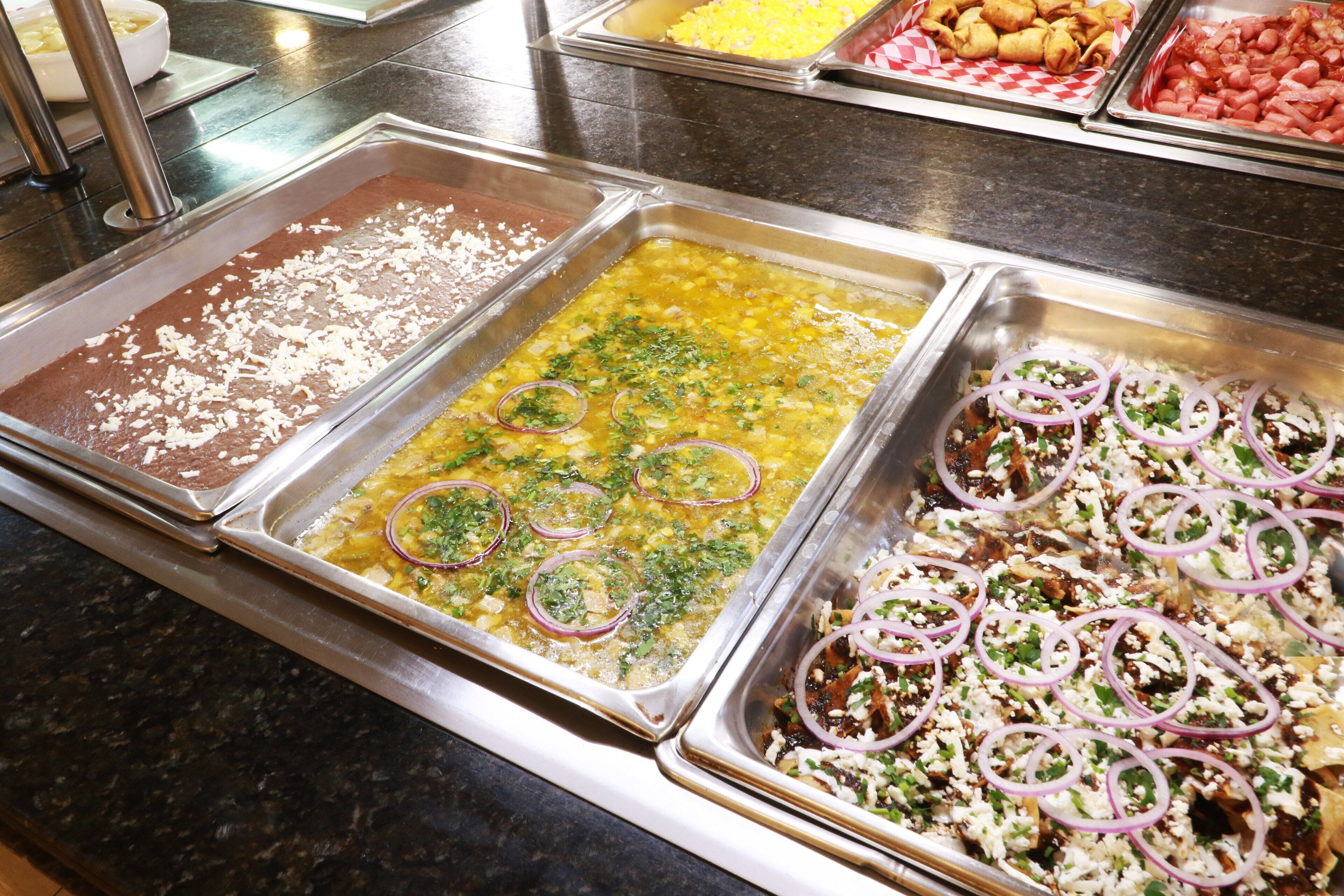A buffet with various dishes including a chocolate dessert, a lentil dish, and a rice dish garnished with onions and herbs.