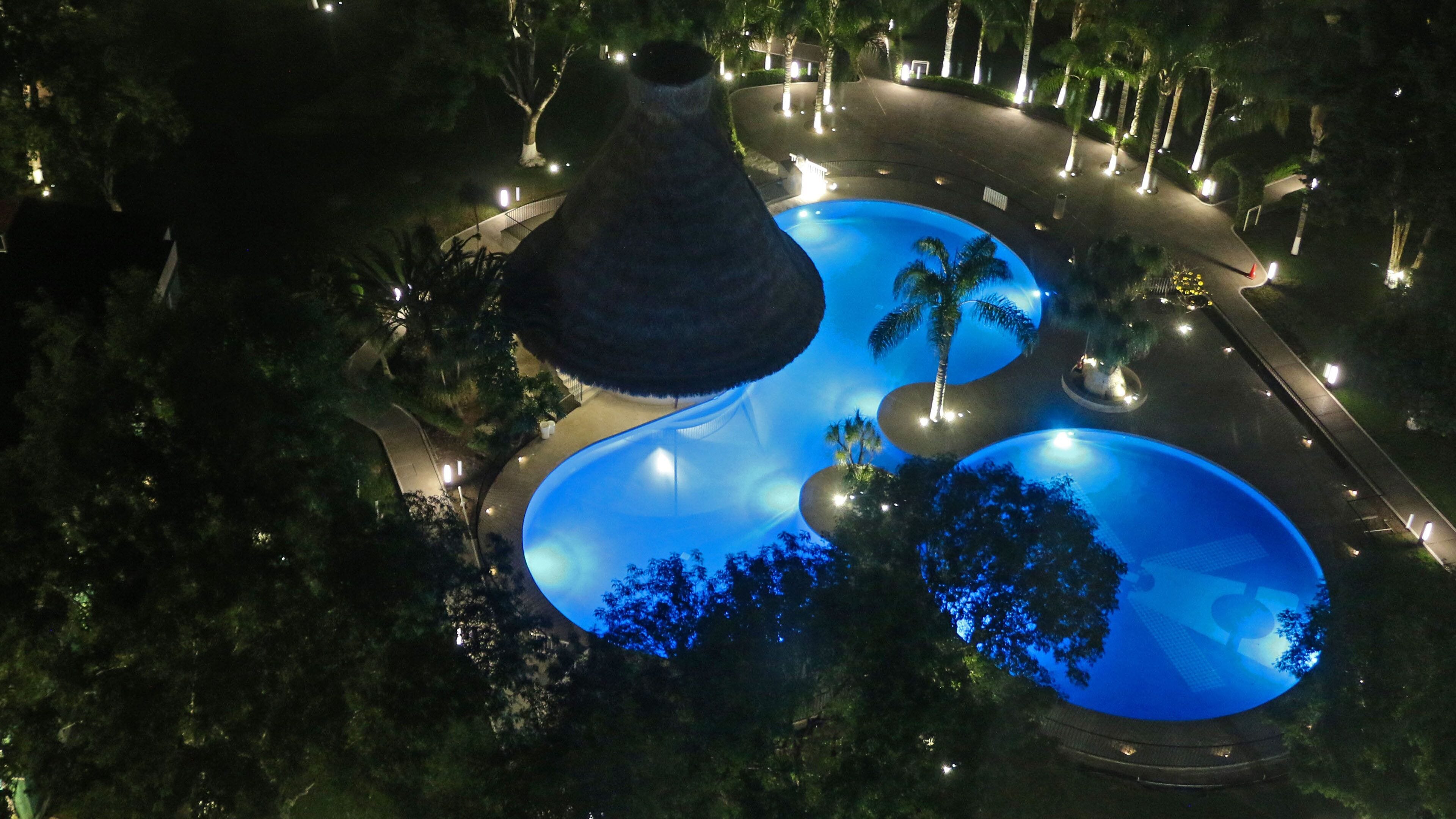 A large, uniquely shaped pool with a conical roof, surrounded by palm trees and well-lit pathways.