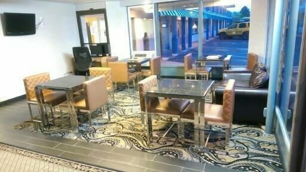 A hotel room with a dining area featuring a glass table and chairs, a patterned carpet, and a view of the street outside. - Rodeway Inn (Vernal)