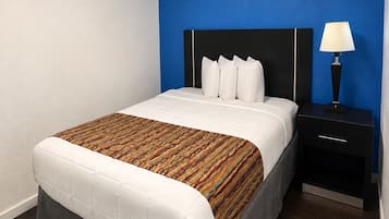 A hotel room with a bed, a nightstand, a lamp, and a blue accent wall.