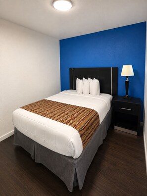 Une chambre d’hôtel avec un lit, une table de chevet, une lampe et un mur d’accent bleu.
