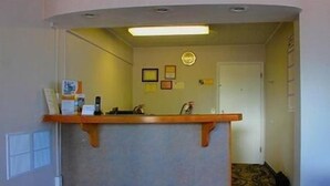 A reception desk with a counter, a phone, and a small table with a sign. There are framed pictures on the wall and a door in the background. - Rodeway Inn (Vernal)