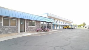 A motel with a blue roof, stone facade, and a parking lot with a yellow vehicle. - Rodeway Inn (Vernal)