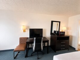 Habitación de hotel con cama, escritorio con televisor, silla, banco, cómoda y espejo.