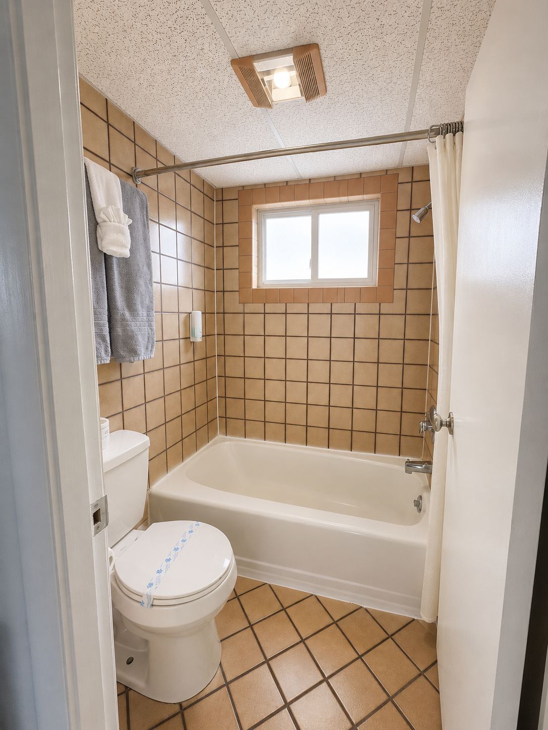 A bathroom with a bathtub, toilet, and a window above the shower area.