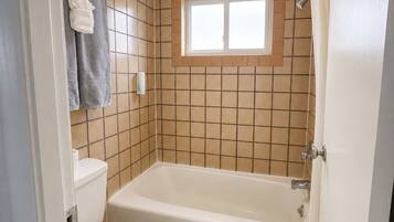 A bathroom with a bathtub, toilet, and a window above the shower area.