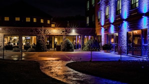 Een hotelentree met een stenen gevel, terras en een goed verlicht pad.