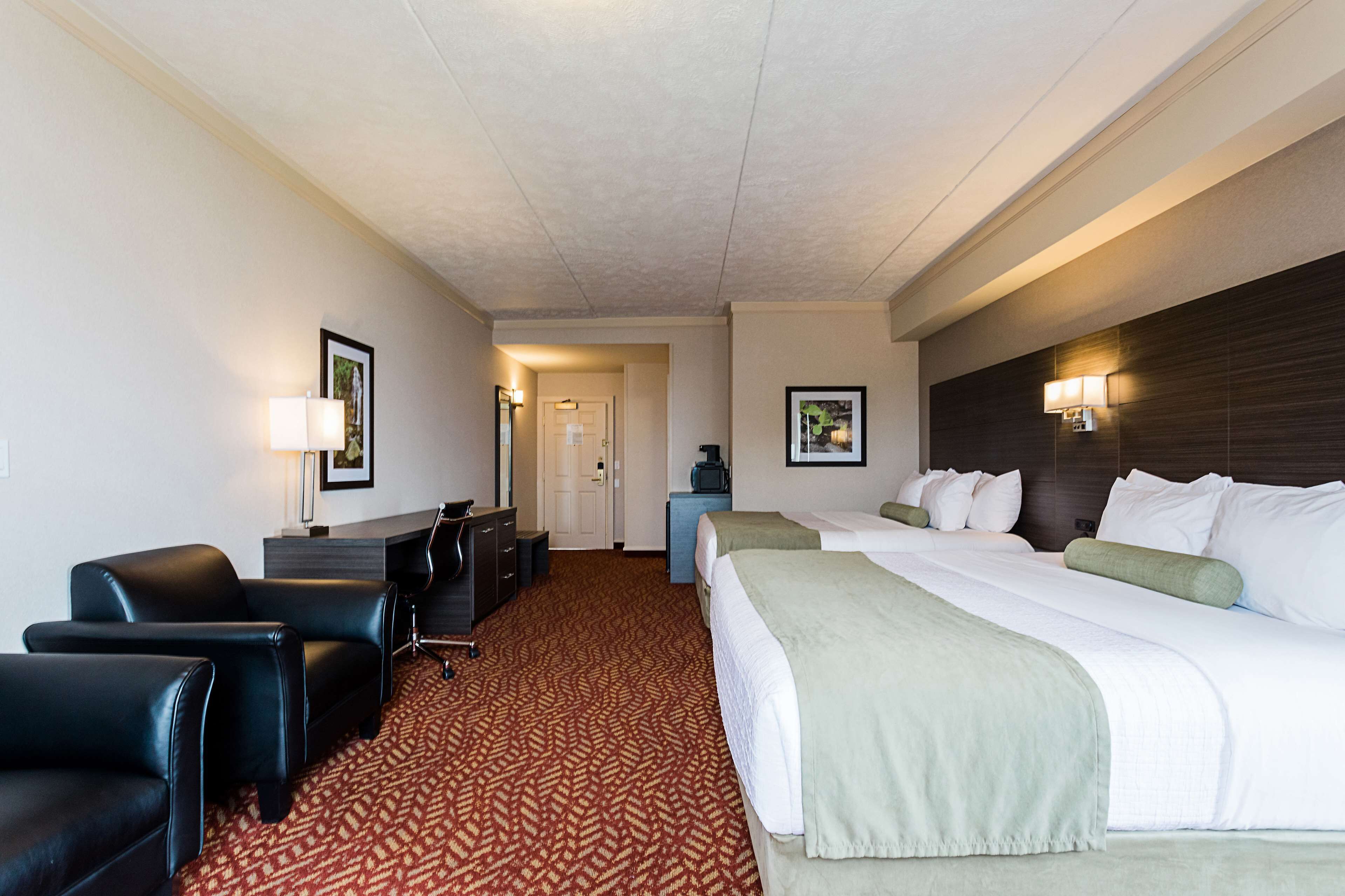 Une chambre d’hôtel comprenant un lit, deux fauteuils, un bureau et un téléviseur.
