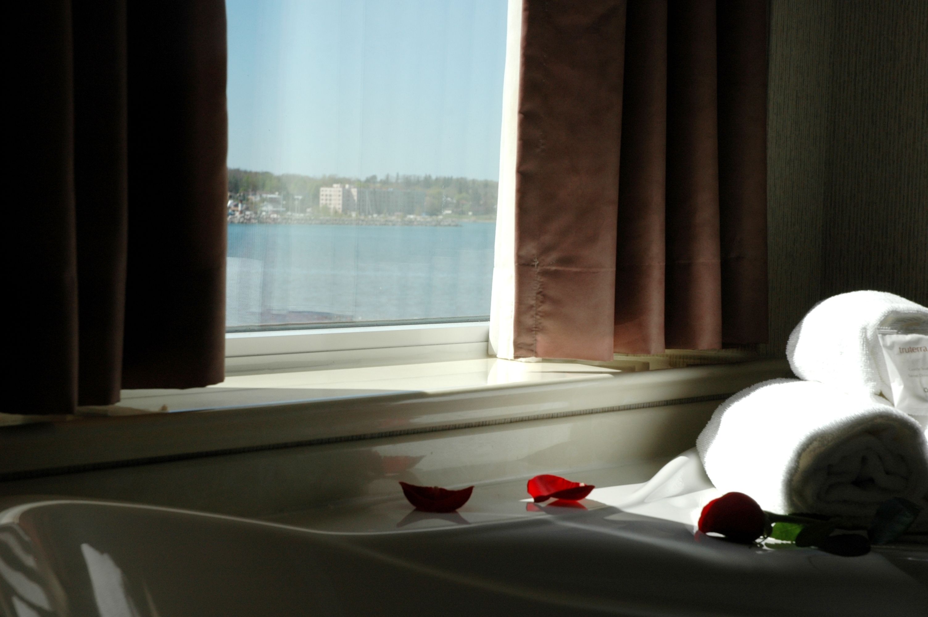 A hotel room with a bed, a window with curtains, and a view of a body of water and buildings.