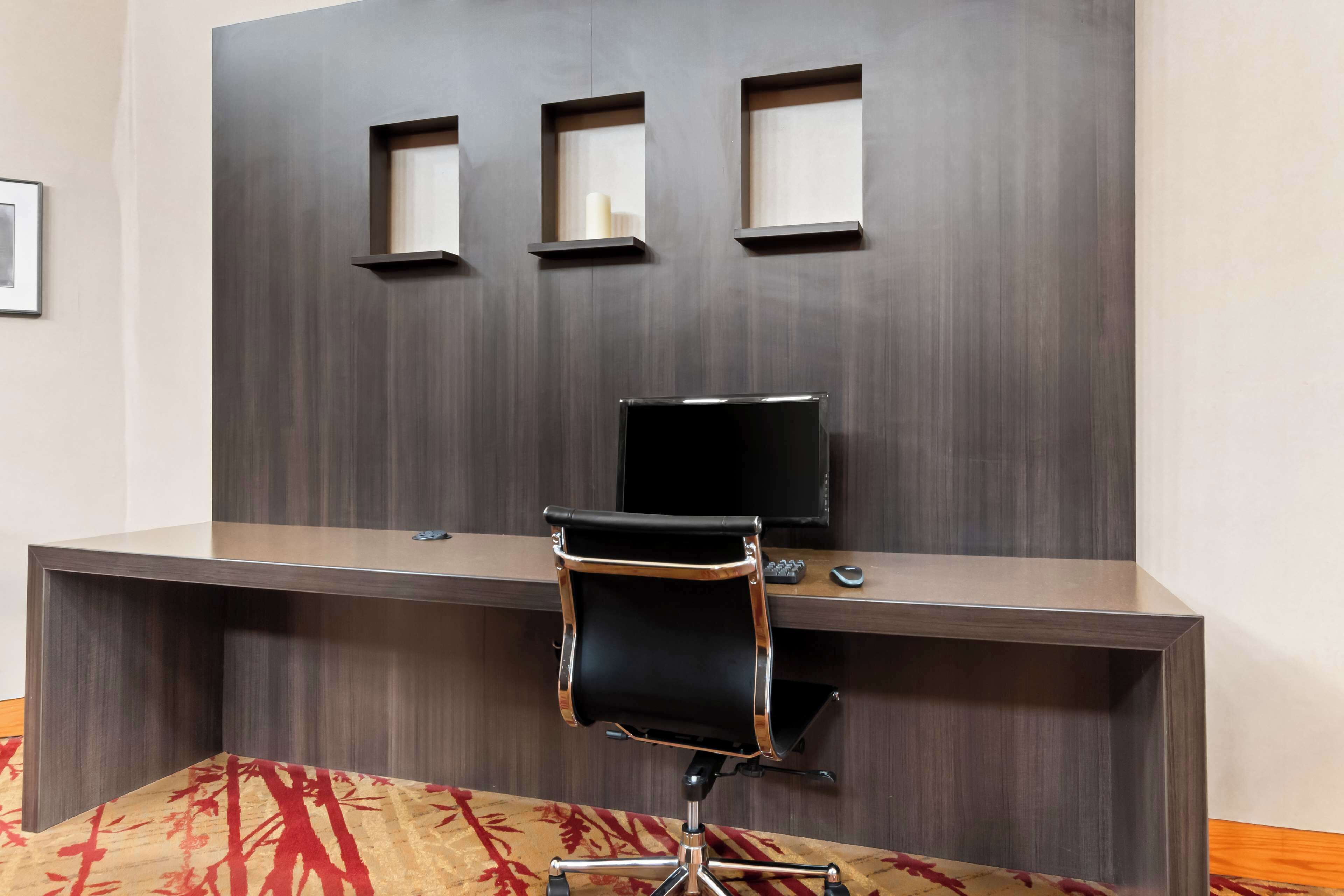 Un bureau moderne doté d’un écran plat, d’un fauteuil de bureau noir et de trois étagères fixées au mur.