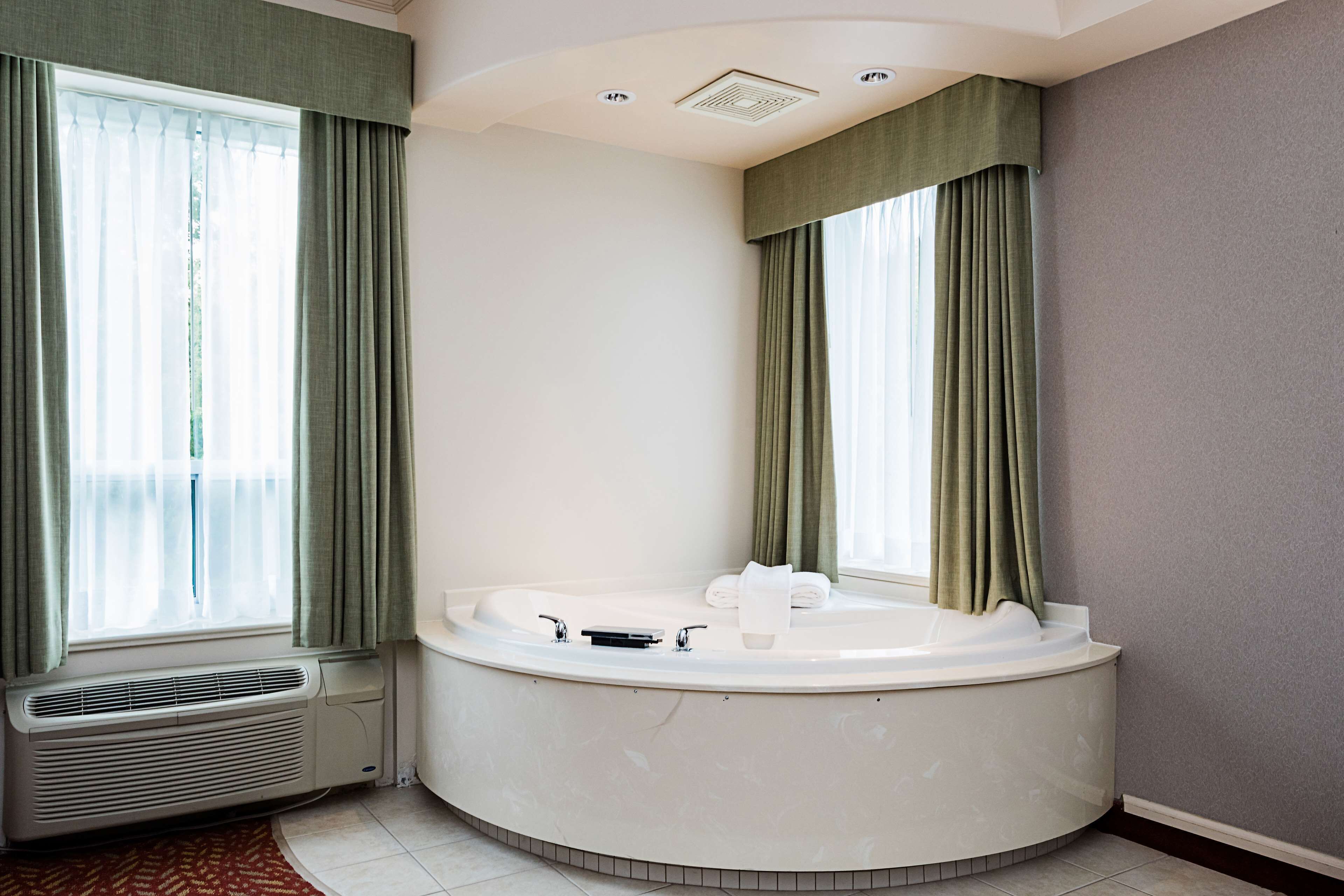 Un baño moderno con una bañera independiente, un calentador integrado y ventanas amplias con cortinas.