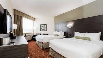 A hotel room with two beds, a desk, a television, and a framed picture on the wall.