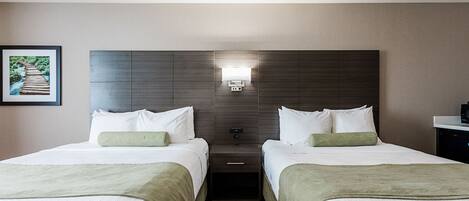 A hotel room with two beds, a nightstand with a lamp, a framed picture on the wall, and a carpeted floor.