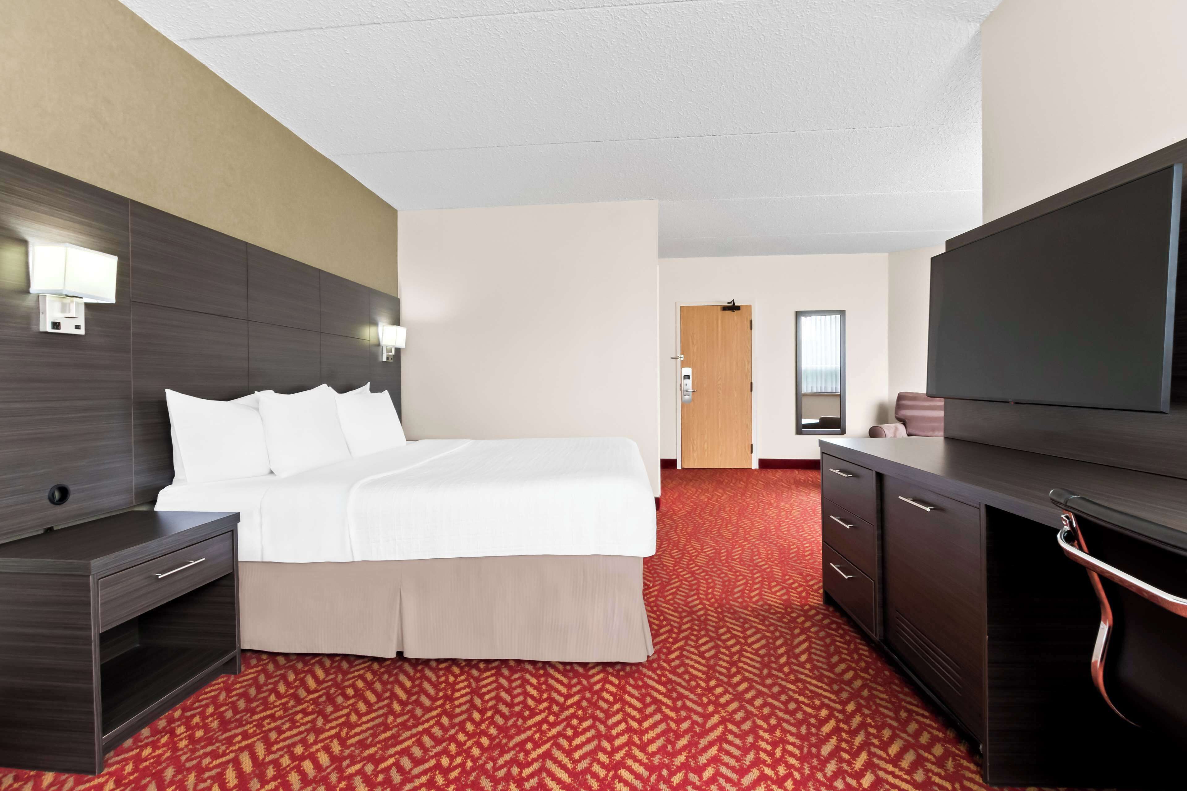 Una habitación de hotel con cama, escritorio, televisión, armario y una puerta que da a otra habitación.