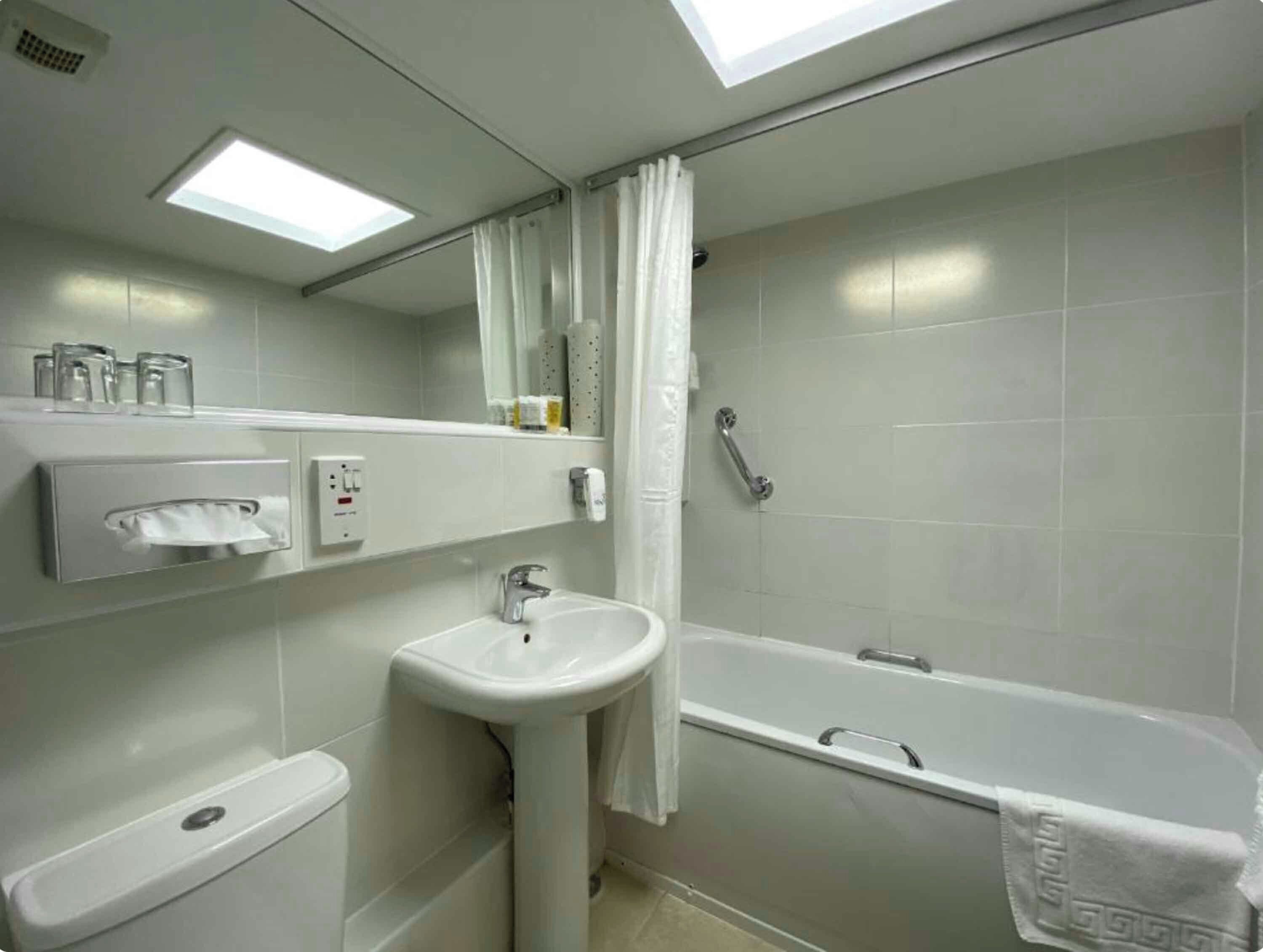 A bathroom with a sink, toilet, and bathtub. There is a mirror above the sink and a shower curtain.