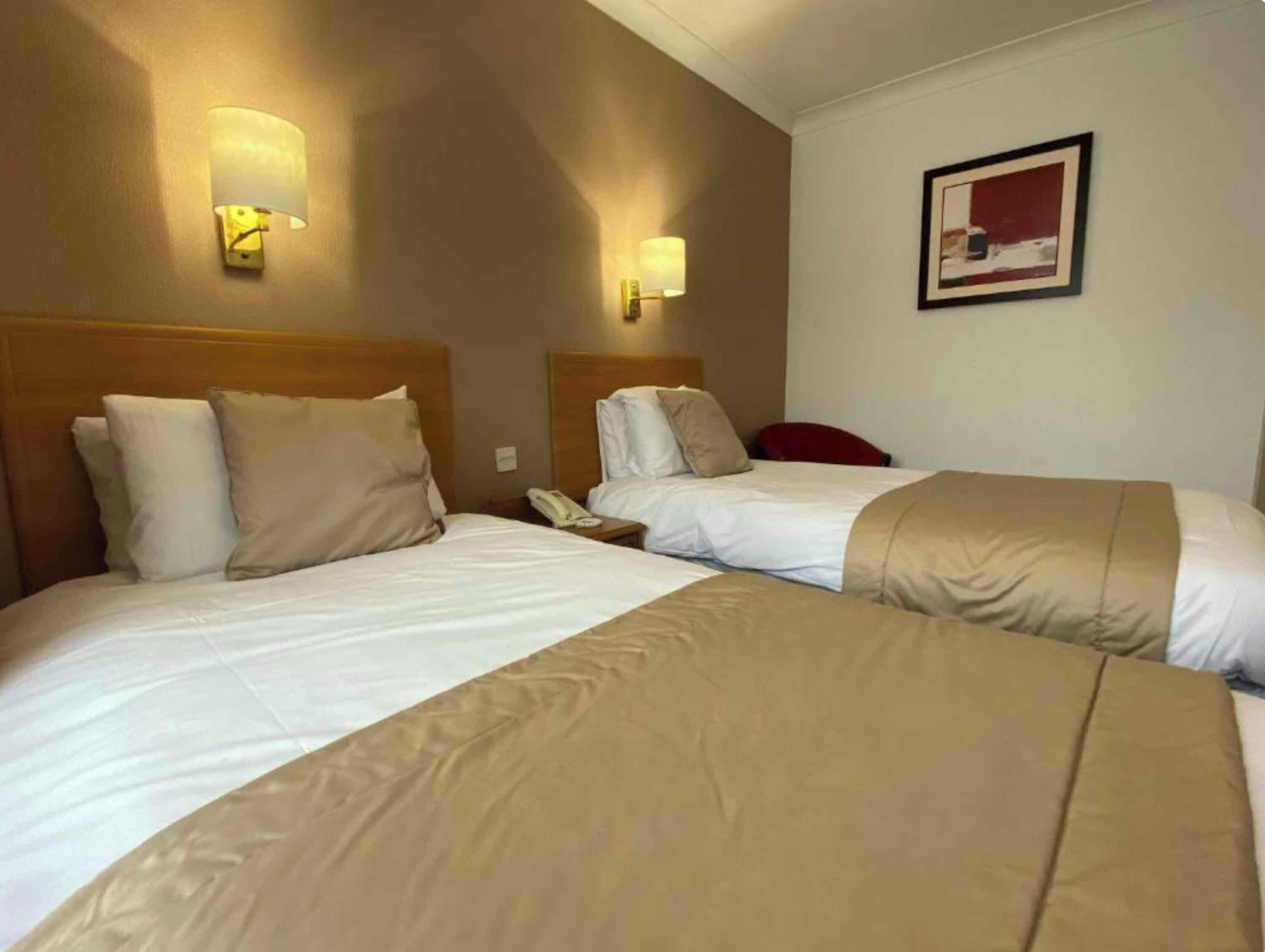 A hotel room with two beds, each with a headboard, a bedside table, a lamp, and a telephone.
