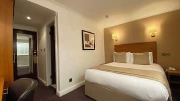 Un cuarto de hotel con una cama grande, un escritorio, una silla, un cuadro en la pared y una puerta que da a otra habitación.