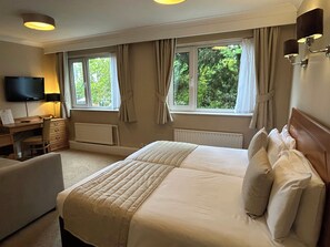A hotel room with a bed, a desk, a chair, a television, and windows with curtains. - The Great Barr Hotel (Birmingham)